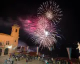 Spettacolo pirotecnico illumina il cielo notturno per la festa di San Marino. Folla ammira i fuochi d'artificio da una piazza con un edificio storico.