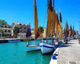 Barche a vela ormeggiate in un porto con case colorate sullo sfondo. Un dilemma: meglio Bellaria o Igea Marina?