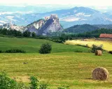 Campagna con borghi vicino Rimini, colline verdi, balle di fieno e un castello arroccato su uno sperone roccioso.