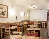 Interno di un ristorante accogliente, con tavoli apparecchiati e sedie colorate. Sembra proprio il posto ideale per una cena da "la mi mama Rimini".