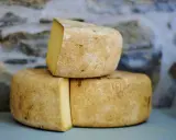 Formaggio Fossa stagionato, con crosta rustica e pasta gialla, impilato su uno sfondo di pietra grezza.