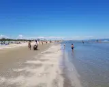 Una giornata di sole a Pinarella di Cervia mare, con bagnanti che passeggiano sulla sabbia e bambini che giocano nell'acqua cristallina.