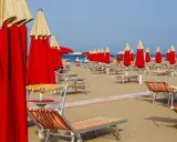 File di ombrelloni rossi e lettini prendisole su una spiaggia, forse a Riccione o Rimini, in attesa dei bagnanti.