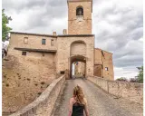 Passeggiata verso il borgo di Montegridolfo cosa vedere: un antico portale in mattoni con torre dell'orologio e un ponte acciottolato.