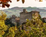 Castello medievale su una collina, circondato da alberi con foglie autunnali dai colori caldi. Il paesaggio collinare sullo sfondo evoca un senso di pace in questo mare autunno.