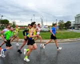 Atleti impegnati nella Rimini Half Marathon, corrono su asfalto bagnato con un cielo nuvoloso.