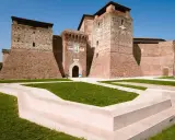 Imponente Castel Sismondo, con le sue torri in mattoni rossi e il cortile verdeggiante, si erge maestoso sotto un cielo azzurro.