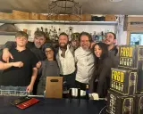 Staff sorridente a Misano Adriatico, con un ragazzo che sembra un gambero sbronzo tra loro. Sul bancone, bottiglie e lattine di "FRGD Irish Stout".