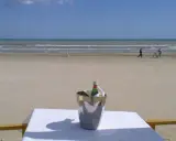 Coppia passeggia sulla spiaggia di Milano Marittima, con un secchiello del ghiaccio e una bottiglia su un tavolo in primo piano.