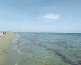 Gente che si gode il sole e il mare a Lido Adriano. Bambini giocano sulla sabbia, adulti nuotano e si rilassano nell'acqua cristallina.