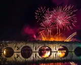 Fuochi d'artificio spettacolari illuminano il cielo notturno sopra un ponte storico, celebrando il capodanno in riviera romagnola.
