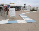 Percorso a strisce bianche e blu sulla sabbia del piazzale San Martino a Riccione, conduce al bar Papaya e alla spiaggia attrezzata.