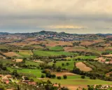 Dolci colline verdi e marroni della Valconca, Rimini, punteggiate da case e alberi, sotto un cielo nuvoloso.