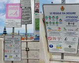 Cartelli informativi su una spiaggia libera attrezzata con regole di distanziamento e norme di comportamento.