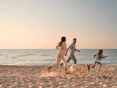 Famiglia e cane corrono felici sulla spiaggia, godendosi le vacanze con il cane al mare.