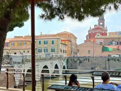 Ponte di Tiberio a Rimini, un luogo iconico per il Rimini Meeting, con persone che passeggiano e ammirano il panorama.