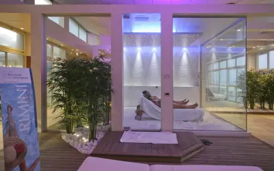 Un'oasi talassoterapico a Rimini, con due persone che si rilassano su lettini in un ambiente moderno e luminoso, circondato da piante di bambù e illuminazione soffusa.