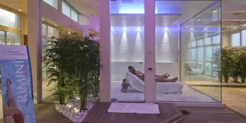 Un'oasi talassoterapico a Rimini, con due persone che si rilassano su lettini in un ambiente moderno e luminoso, circondato da piante di bambù e illuminazione soffusa.