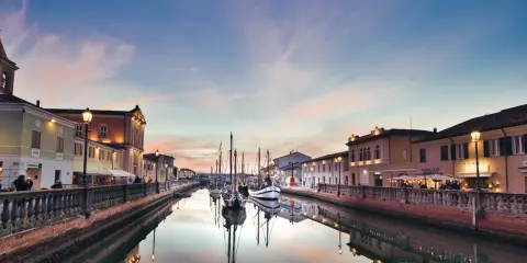 Canale di Cesenatico al tramonto, con barche a vela ormeggiate e riflessi sull'acqua. La riviera cesenatico incanta con i suoi colori.