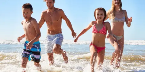 Famiglia corre felice nel mare del lido di Savio, spruzzi d'acqua e sole.