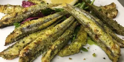 Sardoncini alla romagnola dorati e croccanti, serviti su un letto di insalata fresca con una fetta di limone.