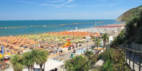 Ampia spiaggia libera a Gabicce Mare, con file infinite di ombrelloni colorati e lettini sotto un cielo azzurro.