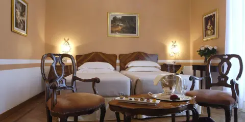 Camera elegante con due letti singoli, un tavolino con champagne e pasticcini, e sedie d'epoca. Un assaggio di lusso al Grand Hotel Rimini.