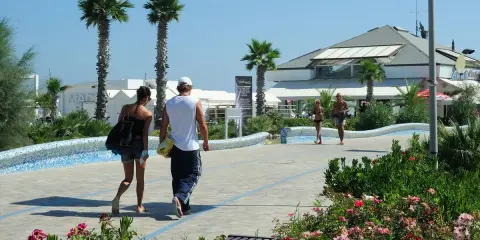 Coppia passeggia sul lungomare del parco mare nord Misano, tra palme e fiori.