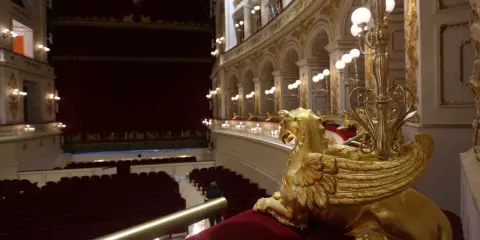 Interno del Teatro Galli di Rimini, con poltrone rosse, palchi dorati e una sfinge alata in primo piano.