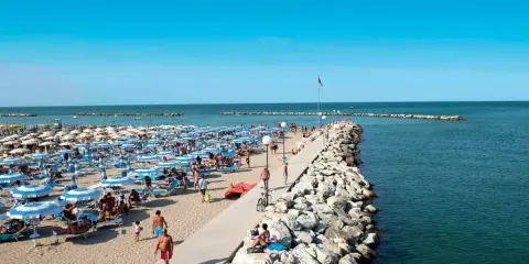Spiaggia affollata a Gatteo Mare Cesenatico, con ombrelloni, lettini e persone che passeggiano sul molo.