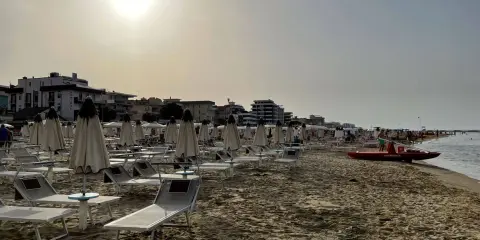 Spiaggia di Igea Marina con lettini e ombrelloni chiusi, bagnino pronto con la sua imbarcazione sul mare calmo.