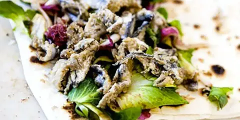 Sardoncini al testo su piadina con insalata fresca e cipolla rossa. Un sapore di mare e terra.