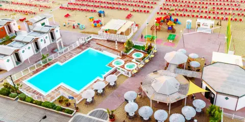 Vista aerea del lido delle sirene Cattolica: piscina, vasche idromassaggio, lettini rossi e ombrelloni sulla spiaggia.