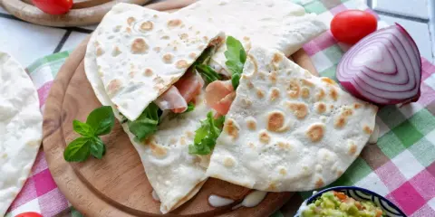 Piadina, piatto tipico di Rimini, farcita con prosciutto e rucola, servita con guacamole e verdure fresche.
