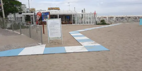 Percorso a strisce bianche e blu sulla sabbia del piazzale San Martino a Riccione, conduce al bar Papaya e alla spiaggia attrezzata.