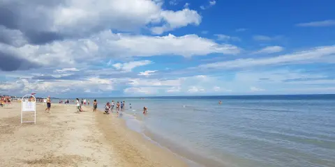 Una giornata di sole sulla spiaggia del cuore Riccione, con bambini che giocano e adulti che si godono il mare calmo sotto un cielo azzurro e nuvoloso.