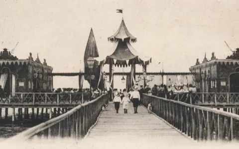 Antica passeggiata sui bagni isola di Cervia, con bambini che camminano sul pontile verso le strutture sul mare.
