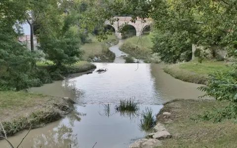 Un fiume serpeggia verso un antico ponte ad archi, evocando il **passaggio del Rubicone**. Vegetazione lussureggiante e acque tranquille.