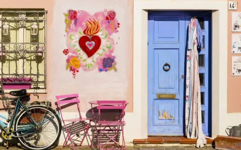 Un angolo pittoresco di Borgo San Giuliano a Rimini: una porta blu, un cuore fiammeggiante dipinto, una bicicletta e sedie rosa.