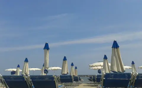 Spiaggia attrezzata al bar Lido di Savio, con lettini blu e ombrelloni bianchi e blu sotto un cielo limpido.
