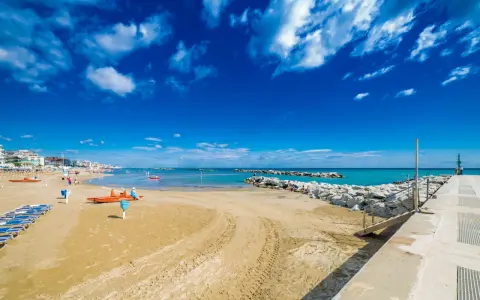 Spiaggia di Bellaria Mare con lettini, bagnini arancioni e mare azzurro sotto un cielo blu con nuvole bianche.