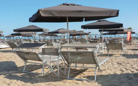 Lettini e ombrelloni scuri sulla sabbia dorata della **Baia degli Angeli Misano**, pronti per accogliere i bagnanti sotto il sole.