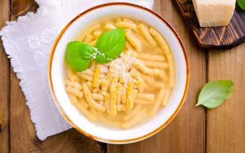 Piatto di passatelli in brodo, un classico dei piatti romagnoli, guarnito con basilico fresco e parmigiano.