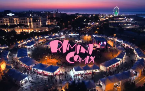 Un vivace evento serale a Rimini Comix, con bancarelle illuminate, una ruota panoramica e il logo rosa che domina la scena.