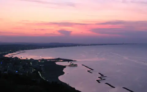 Panoramica Gabicce al tramonto, con cielo rosa e viola, mare calmo e costa illuminata.