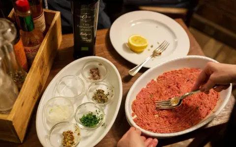 Preparazione di tartare di carne in un ristorante a Rimini, con condimenti e olio EVO.
