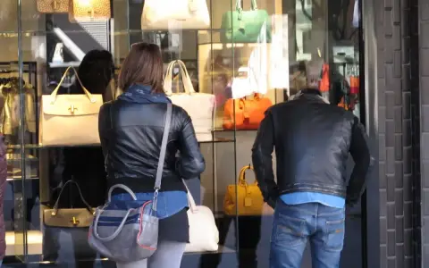 Coppia osserva vetrina di borse Benetton a Riccione. Lei con giacca in pelle, lui con giubbotto.