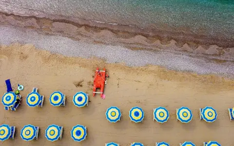 Ombrelloni blu e gialli e una barca rossa sulla spiaggia di Misano Marittima, con il mare turchese sullo sfondo.