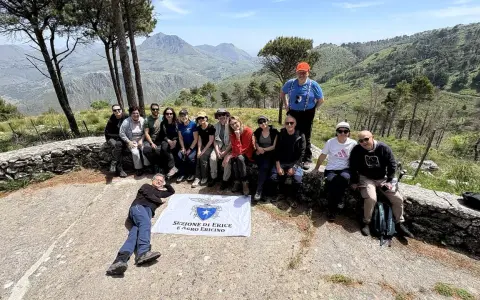 Gruppo di escursionisti con bandiera della Sezione di Erice e Agro Ericino, in cima al monte Gradara, con vista panoramica sulla valle.