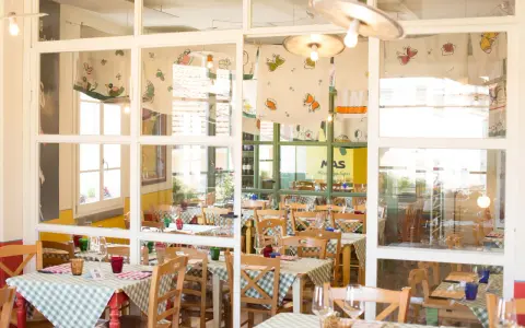 Interno di un'osteria de borg con tavoli apparecchiati con tovaglie a quadretti verdi e bianchi, sedie in legno e decorazioni colorate.